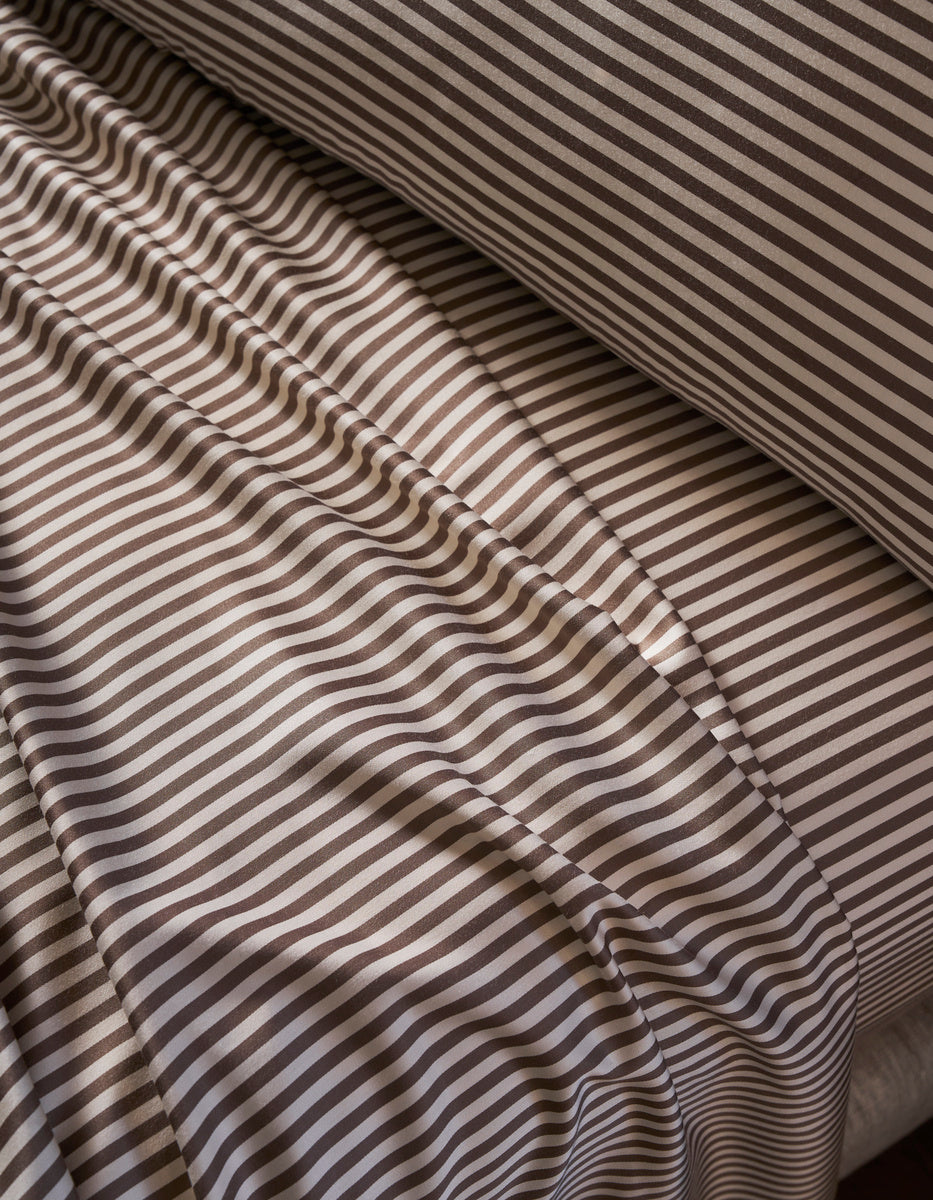 Close-up of the Bamboo Bedding Essential Bundle by Cozy Earth, featuring brown and white striped sheets and pillowcase. The slightly wrinkled fabric creates soft shadows and a wavy pattern on the bed surface.