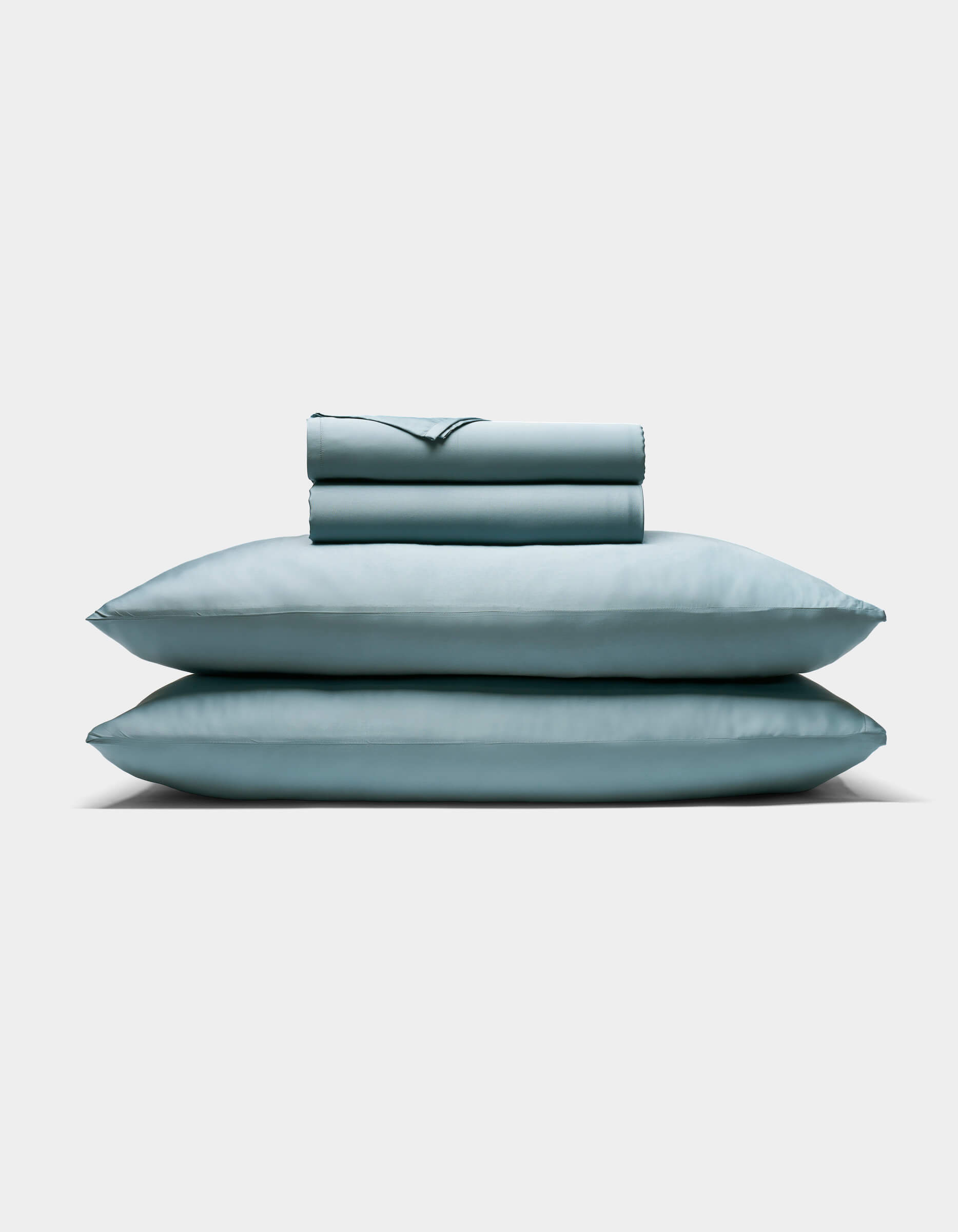 The Cozy Earth Bamboo Sheet Set, featuring two pillows and a folded sheet in pale blue, is neatly stacked against a plain white background.|Color:River