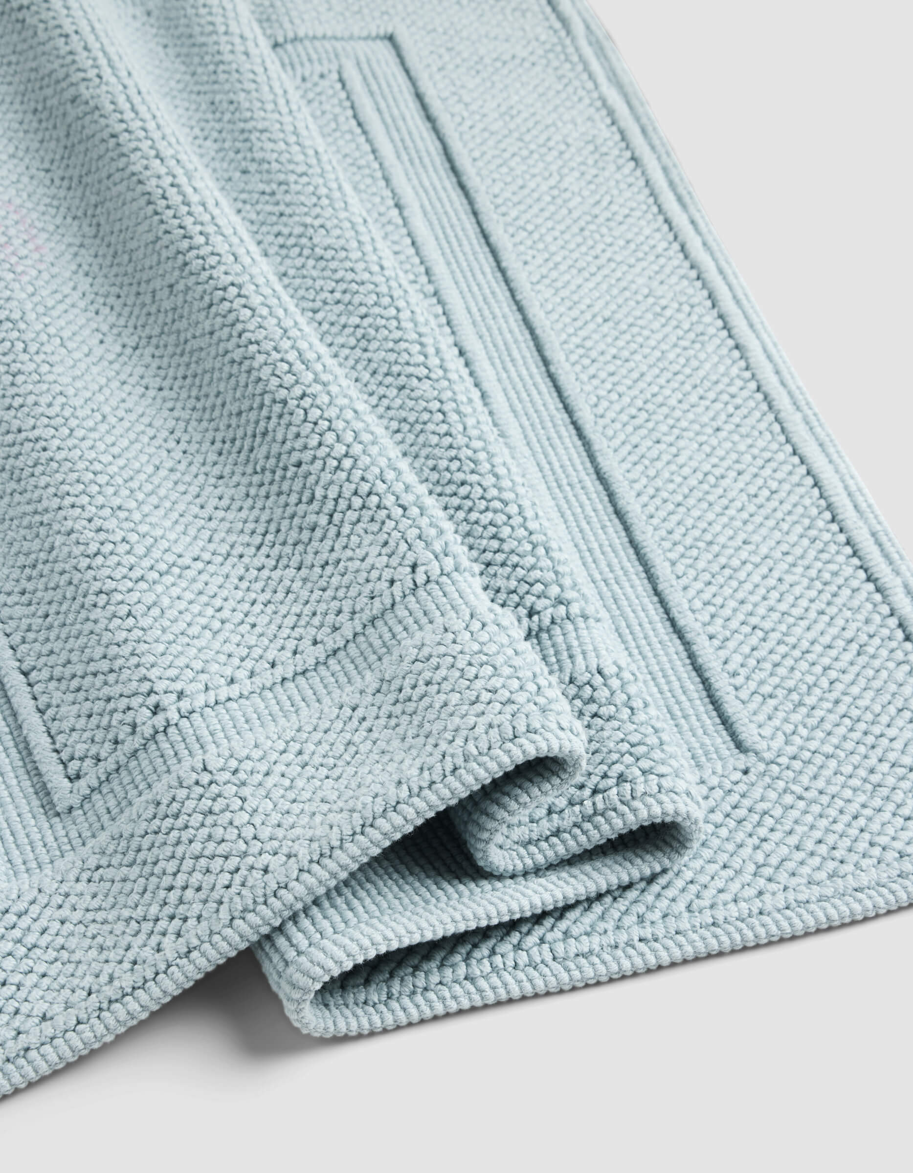 A close-up of the Cozy Earth Classic Bath Mat in light blue, neatly folded to display its textured surface and rectangular border patterns, set against a light gray background.|Color:Harbor Mist